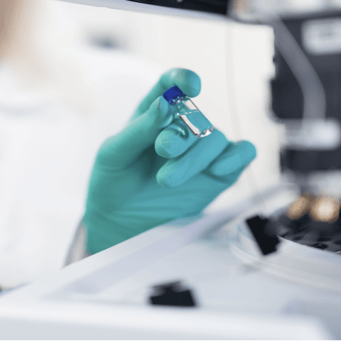Gloved hand inspecting a small vial in a laboratory setting